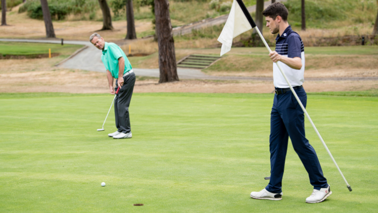 a-golfer-watching-his-putt-on-a-green-next-to-another-golfer-holding-the-flag